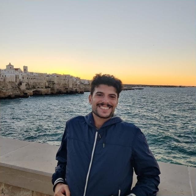 Domenico sorride al tramonto, con il mare e un borgo bianco alle spalle