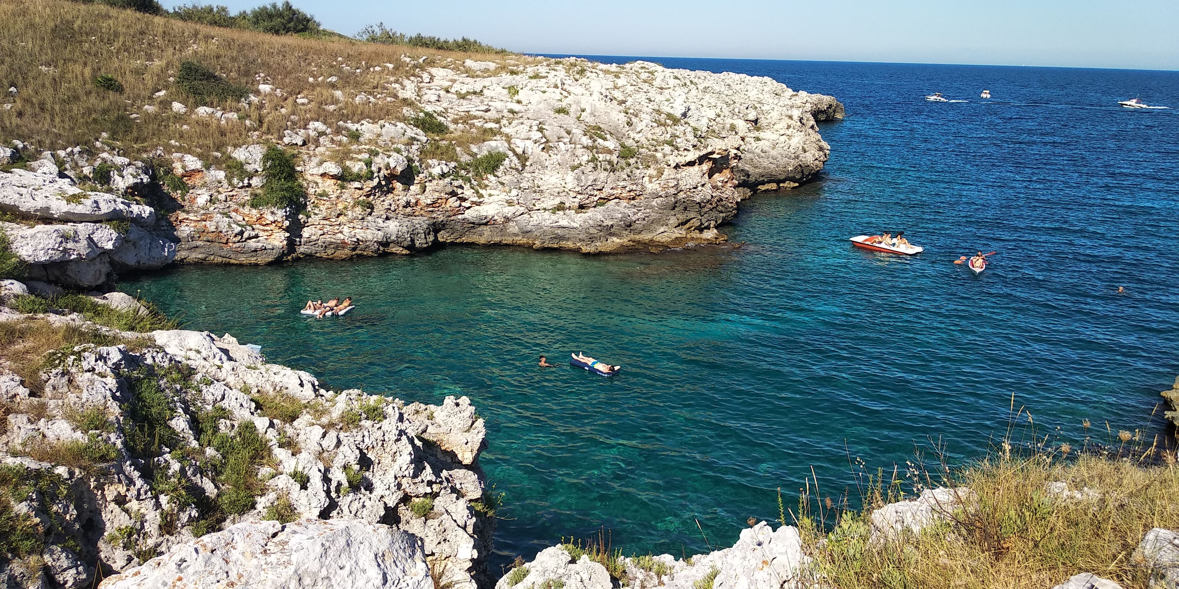 Cala rocciosa del Salento con acqua turchese, persone in acqua e un kayak al largo
